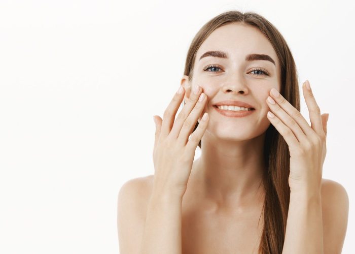 charming-relaxed-gentle-young-woman-making-cosmetological-procedure-applying-facial-cream-face-with-fingers-smiling-broadly-feeling-perfect-taking-care-skin (1)